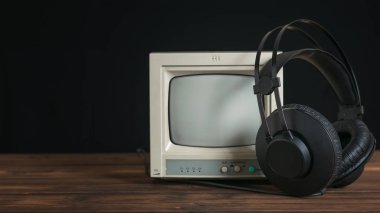 Siyah kulaklıklar, siyah arka plandaki ahşap masada kablo ve retro monitör..