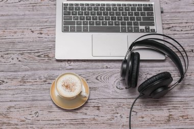 Kablolu siyah kulaklıklar, bir fincan tarçınlı kahve ve ahşap bir masada dizüstü bilgisayar. Görev.