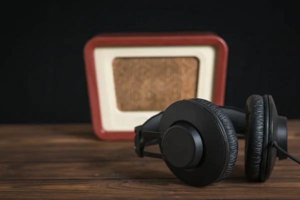 Černá sluchátka s drátem a retro rádio na dřevěném stole na černém pozadí. — Stock fotografie