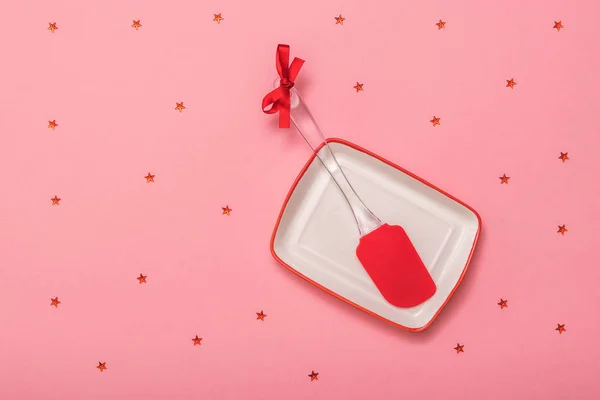 Espátula de cocina roja en un tazón blanco sobre un fondo rojo con estrellas. Puesta plana . — Foto de Stock