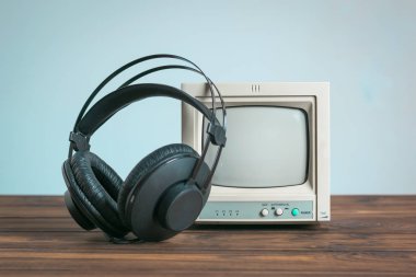 Kulaklıklar, mavi arka plandaki ahşap bir masada eski bir monitörün yanında..