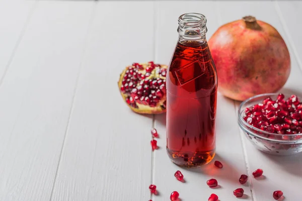 Bouteille en verre de jus de grenade avec des fruits de grenade mûrs sur une table blanche . — Photo