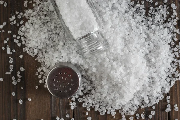 En öppen saltskakare på en hög med spillt salt på ett träbord. — Stockfoto