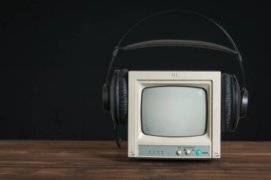 Siyah arka plandaki ahşap masada kulaklık takılı mini retro televizyon..