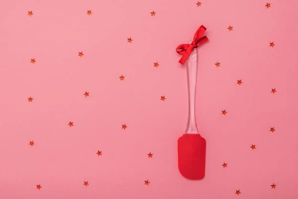 Espátula de cocina roja brillante decorada con cinta roja sobre fondo rosa con estrellas. Puesta plana . — Foto de Stock