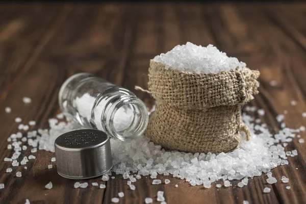 Мішок розкиданої солі і скляний соляний шейкер на дерев'яному столі . — стокове фото