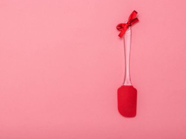 Pembe arka planda kırmızı kurdeleli mutfak spatulası. Düz yatıyordu.