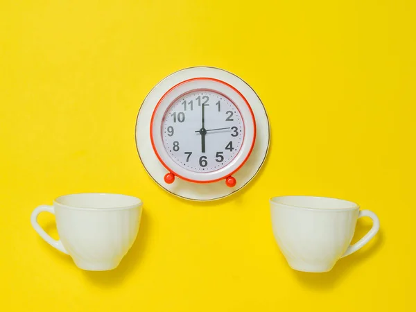 Красный будильник на блюдце и две чашки кофе на желтом фоне. Плоский лежал . — стоковое фото