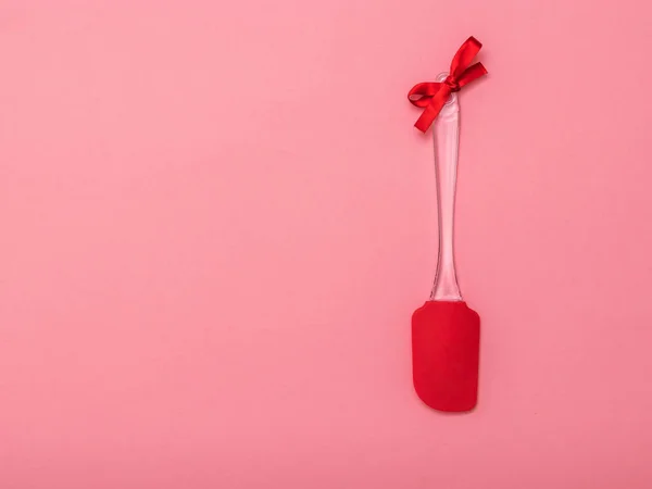 Espátula de cocina con una cinta roja sobre un fondo rosa. Puesta plana . — Foto de Stock