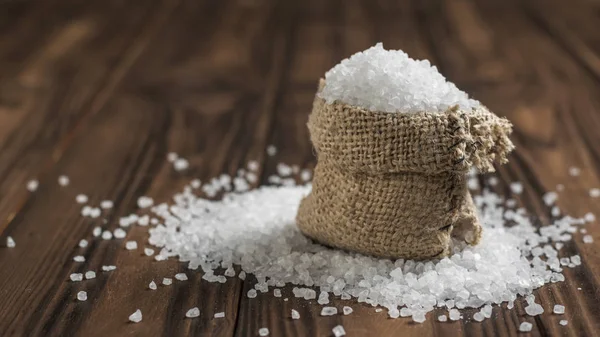 Um saco rasgado de sal em ruínas numa mesa de madeira . — Fotografia de Stock