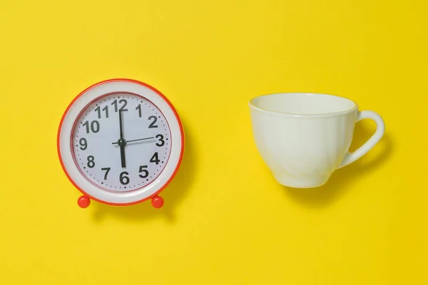 Coffee Cup and white analog alarm clock on yellow background. Flat lay. — Stock Photo, Image