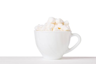 Beyaz arka planda beyaz bir masada sapı olan beyaz bir kasede marşmelov..