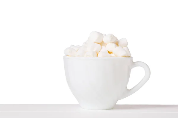 Marshmallow em uma tigela branca com uma alça em uma mesa branca isolada em um fundo branco . — Fotografia de Stock