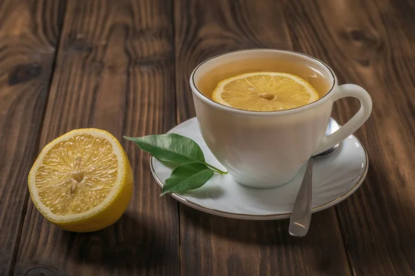 Té con rodajas de limón en una taza blanca sobre una mesa de madera . — Foto de Stock