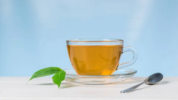 Copa de vidrio con té y hojas verdes sobre una mesa blanca sobre un fondo azul . —  Fotos de Stock