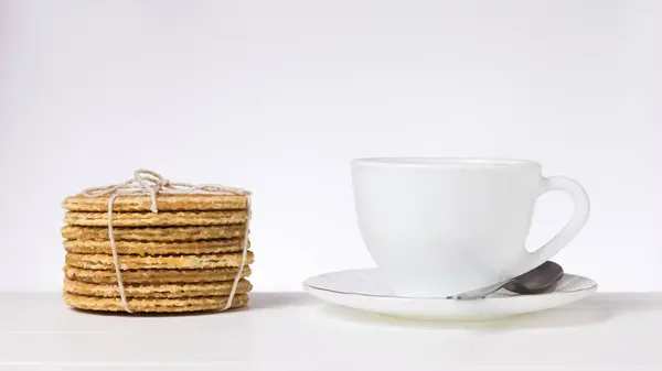 Copa blanca y platillo y gofres caseros sobre la mesa sobre un fondo claro . — Foto de Stock