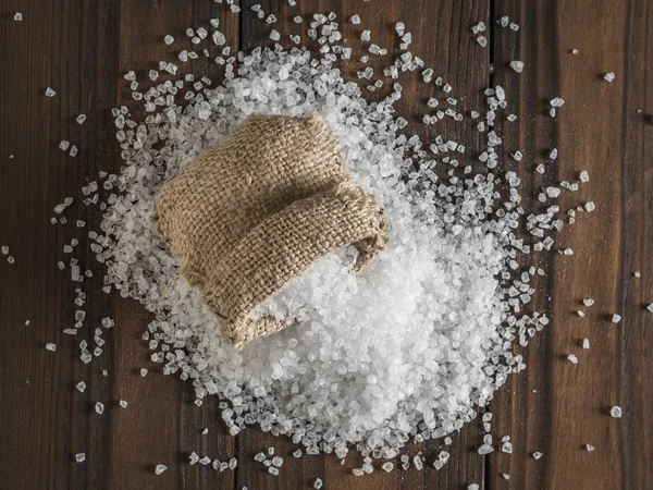 Una bolsa rota de sal marina gruesa esparcida sobre una mesa de madera. Puesta plana . — Foto de Stock