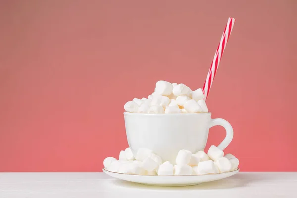 A coffee Cup with a saucer filled with marshmallows and a red tube on a red background. — Stock Photo, Image