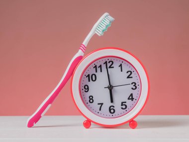 Kırmızı alarm saati ve pembe arka planda beyaz bir masada kırmızı diş fırçası. Sabah konsepti.