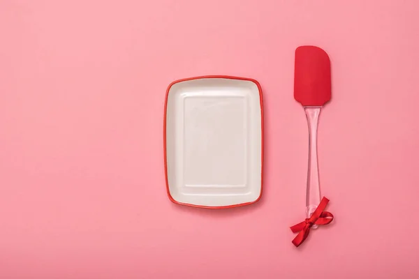 Прямоугольная тарелка и кухонная лопатка на розовом фоне. Плоский лежал . — стоковое фото