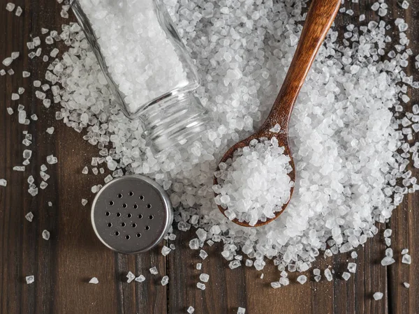 Rozsypana duża sól morska z drewnianą łyżką i solniczką. — Zdjęcie stockowe