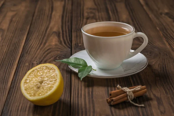 A Cup of fresh tea with half a lemon and cinnamon sticks on a wooden table. — Stock Photo, Image