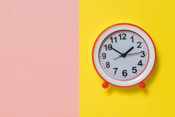 นาฬิกาปลุกแบบอะนาล็อกที่มีลูกศรบนพื้นหลังสีเหลืองและสีชมพู . — ภาพถ่ายสต็อก