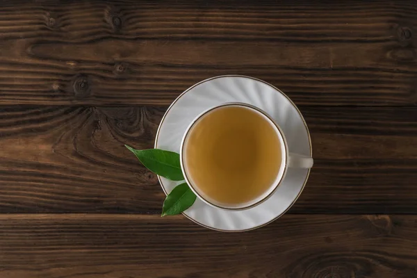 Filiżanka świeżej herbaty, spodek i dwa liście na drewnianym stole. Układy płaskie. — Zdjęcie stockowe