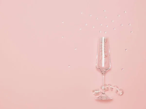 Elegante copa de champán con serpentina y lentejuelas luminosas sobre fondo rosa . — Foto de Stock