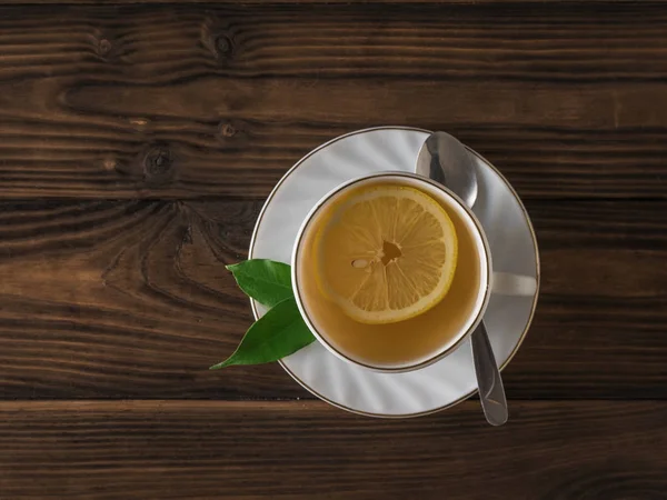 Kawałek cytryny w białej filiżance herbaty i metalowej łyżeczce na drewnianym stole. Układy płaskie. — Zdjęcie stockowe