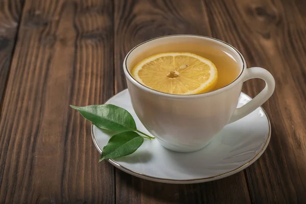 Una rebanada de limón en una taza de té blanca sobre una mesa de madera . — Foto de Stock