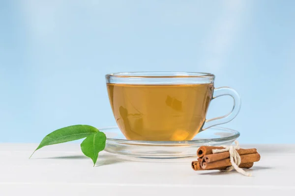 Palitos de canela y té con hojas verdes sobre una mesa blanca sobre un fondo azul . —  Fotos de Stock