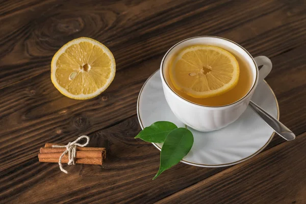 Canela y limón y una taza de té sobre una mesa de madera . — Foto de Stock