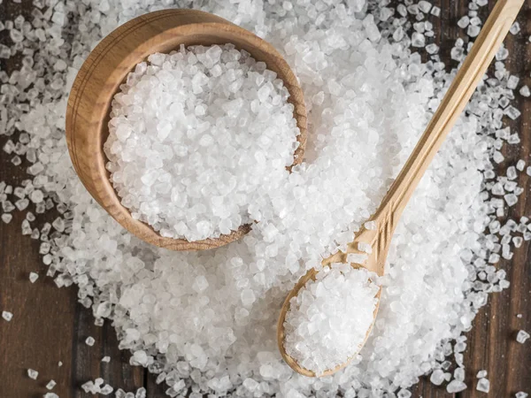 Un sacco di sale sparso con una tazza di legno e cucchiaio sul tavolo. Posa piatta . — Foto Stock