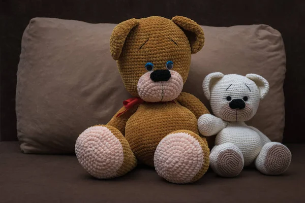 Big and small knitted bears sitting in an embrace on the sofa.