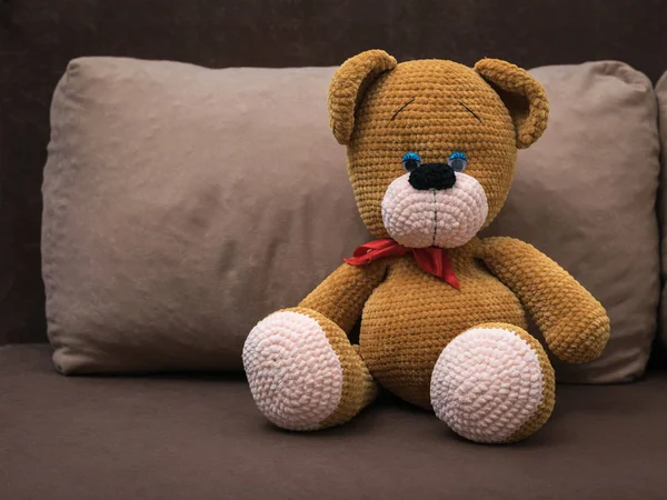 A large knitted bear with a red headband on a soft sofa.