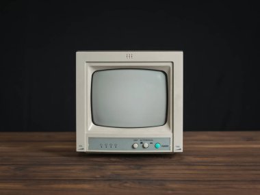 Siyah arka planda tahta bir masada küçük bir retro monitör..