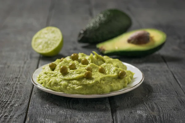 A plate of guacamole with green peas and avocado fruit on a wooden table. Diet vegetarian Mexican food avocado. — Stock Photo, Image
