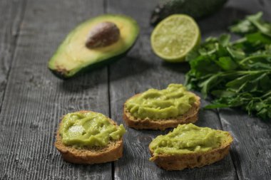 Siyah ahşap bir masanın üzerinde guacamole soslu üç dilim ekmek. Diyet vejetaryen Meksika yemeği avokadosu..
