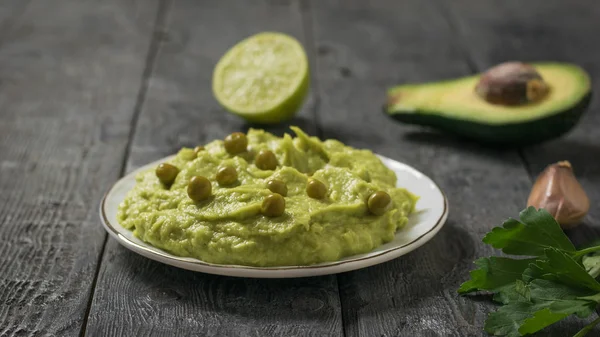 Гуакамоле с зеленым горошком в белой тарелке и травами. Мексиканская вегетарианская еда авокадо . — стоковое фото