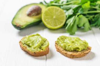 Beyaz ahşap bir masada guacamole soslu iki ince ekmek dilimi. Diyet vejetaryen Meksika yemeği avokadosu..