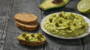 Siyah ahşap bir masada guacamole ve yeşil bezelye ile tam tahıllı ekmek. Diyet vejetaryen Meksika yemeği avokadosu..