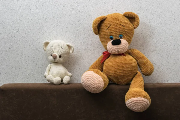 Two sad knitted bear cubs on the sofa against the light wall.