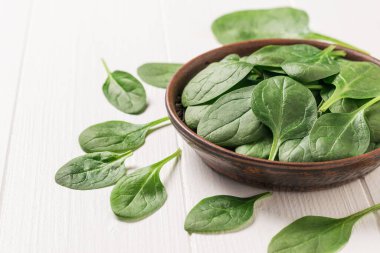 Beyaz ahşap bir masada ıspanak yapraklı bir kil kase. Zindelik için yemek.