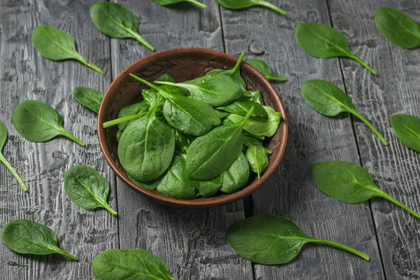 Spinach leaves in a clay bowl and on a black wooden table. Food for fitness. The view from the top. — Stock Photo, Image