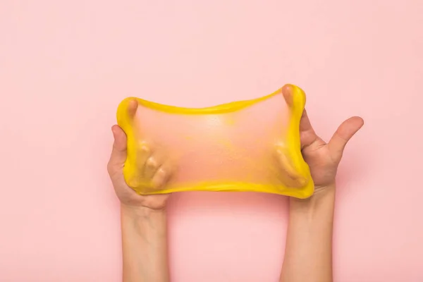 Натянутая до прозрачности желтая слизь в руках на розовом фоне . — стоковое фото