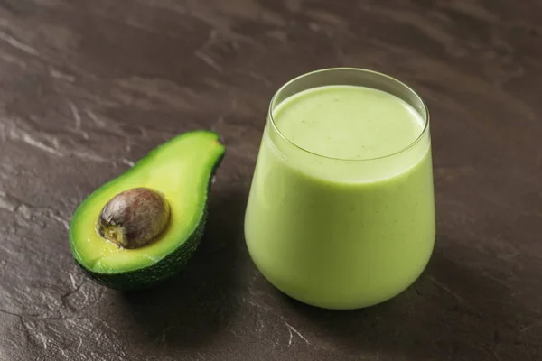 Ein Glas Avocado- und Spinat-Smoothies und eine halbe Avocado auf Steingrund. Fitness-Produkt. — Stockfoto