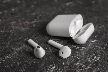 White wireless headphones with charging case on black stone background.