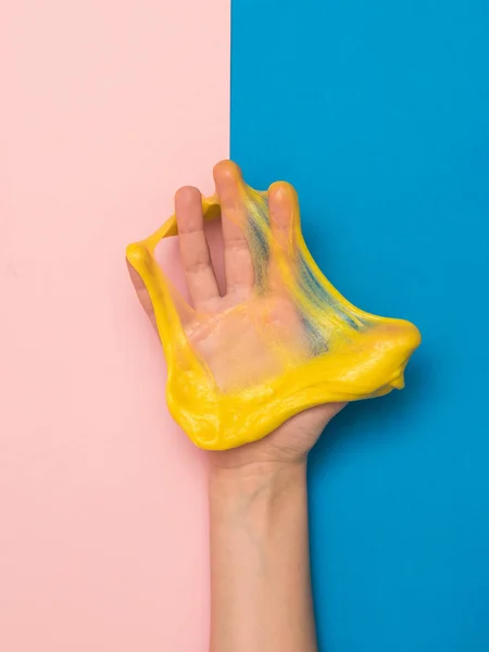 Пальцы правой руки ломают желтую слизь на розовом и синем фоне . — стоковое фото