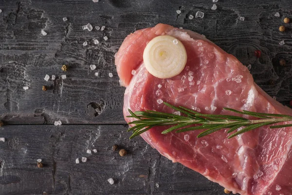 Um pedaço de porco com sal e especiarias e cebolas em uma mesa de madeira . — Fotografia de Stock